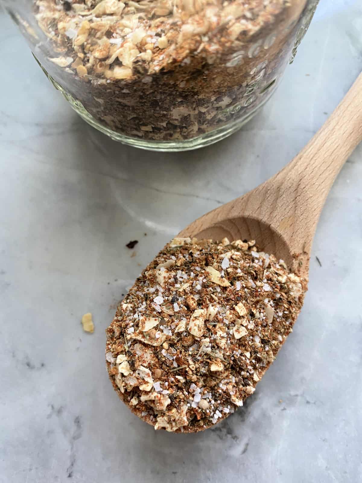 Top view of a wooden spoon filled with spices and a jar next to it.