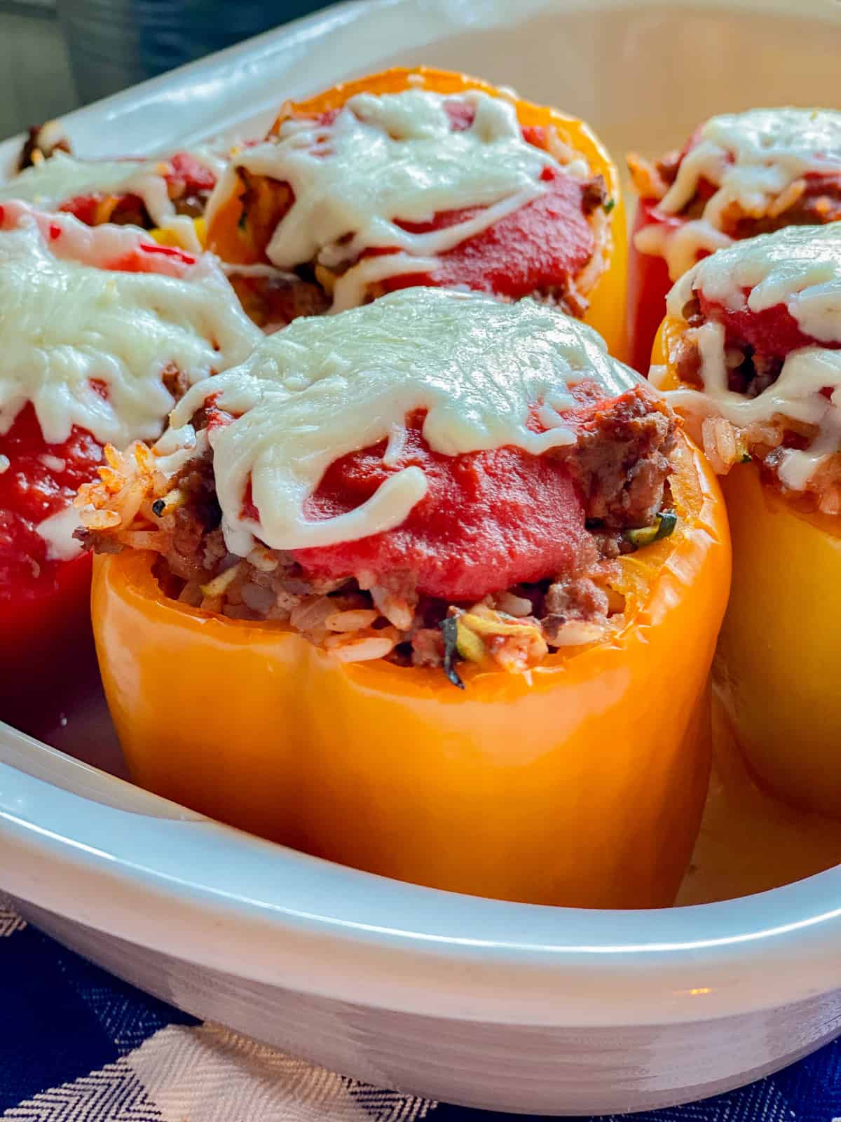close up of orange stuffed peppers with red sauce and white cheese.