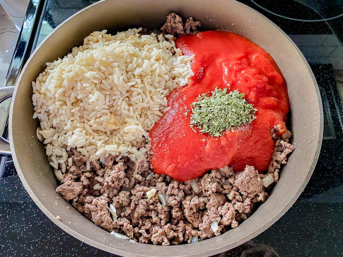 skillet with cooked ground beef with red tomato sauce and white rice with green seasoning.