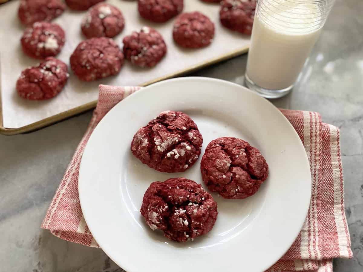 Three red cookies on a white plate with milk on the side.