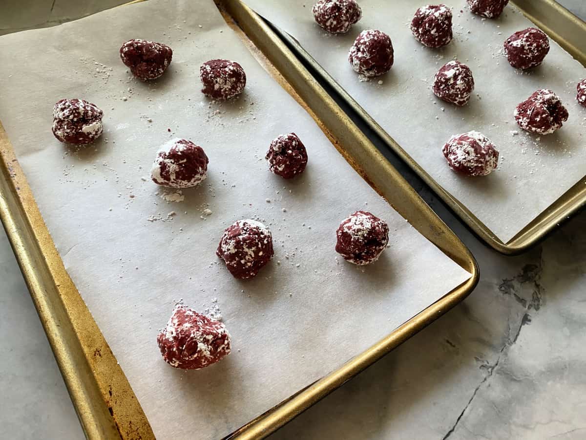 Two baking trays with round red cookie dough balls.