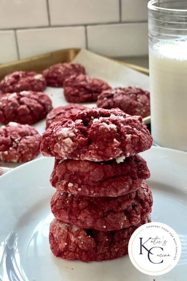 Four red cookies stacked on top of each other on a white plate with a log on the right corner of the photo.