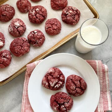 Top view of a baking sheet and white plate filled with red cookies.