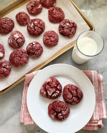 Top view of a baking sheet and white plate filled with red cookies.