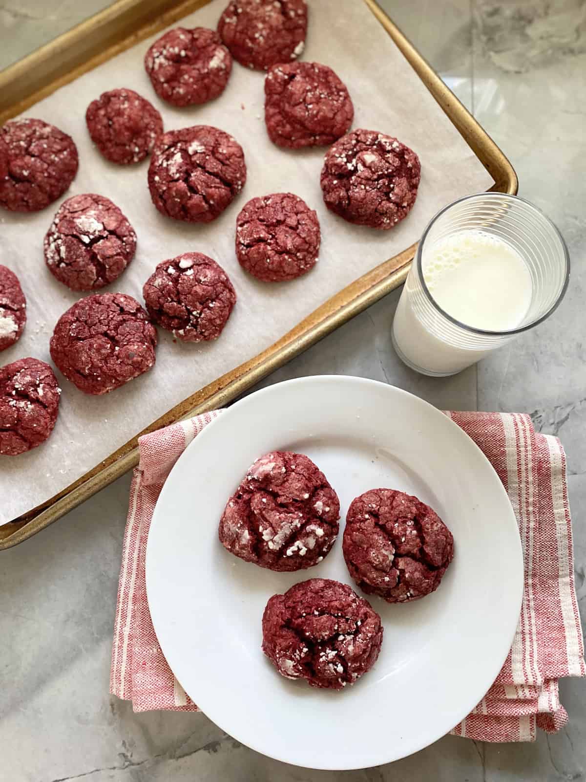 Top view of a baking sheet and white plate filled with red cookies.