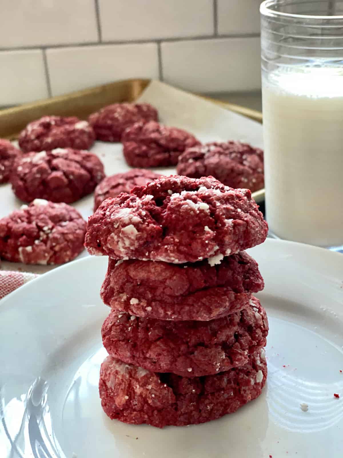 Four red cookies stacked on a white plate next to milk.