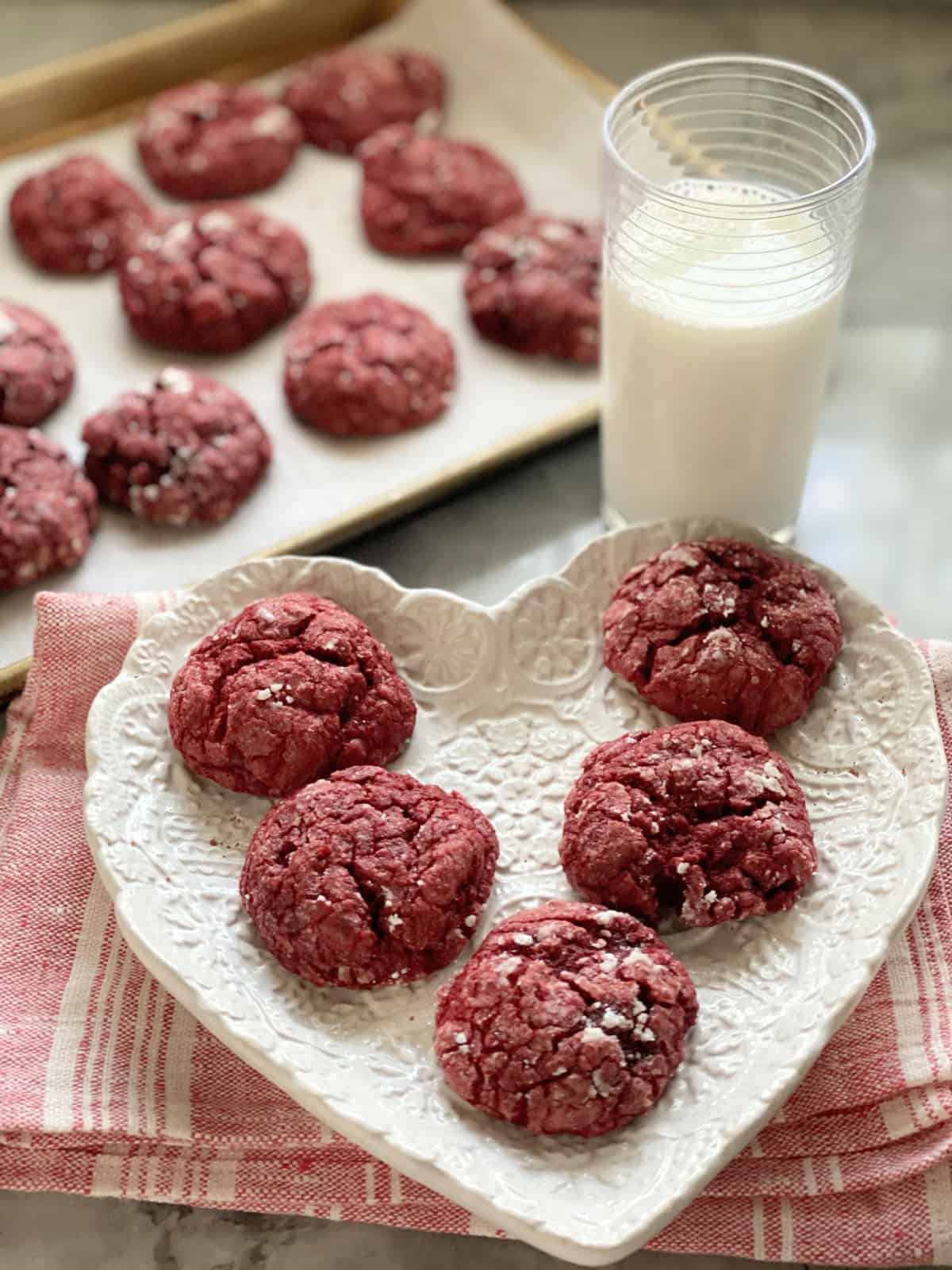 White heart shaped plate with five red cookies resting on it.