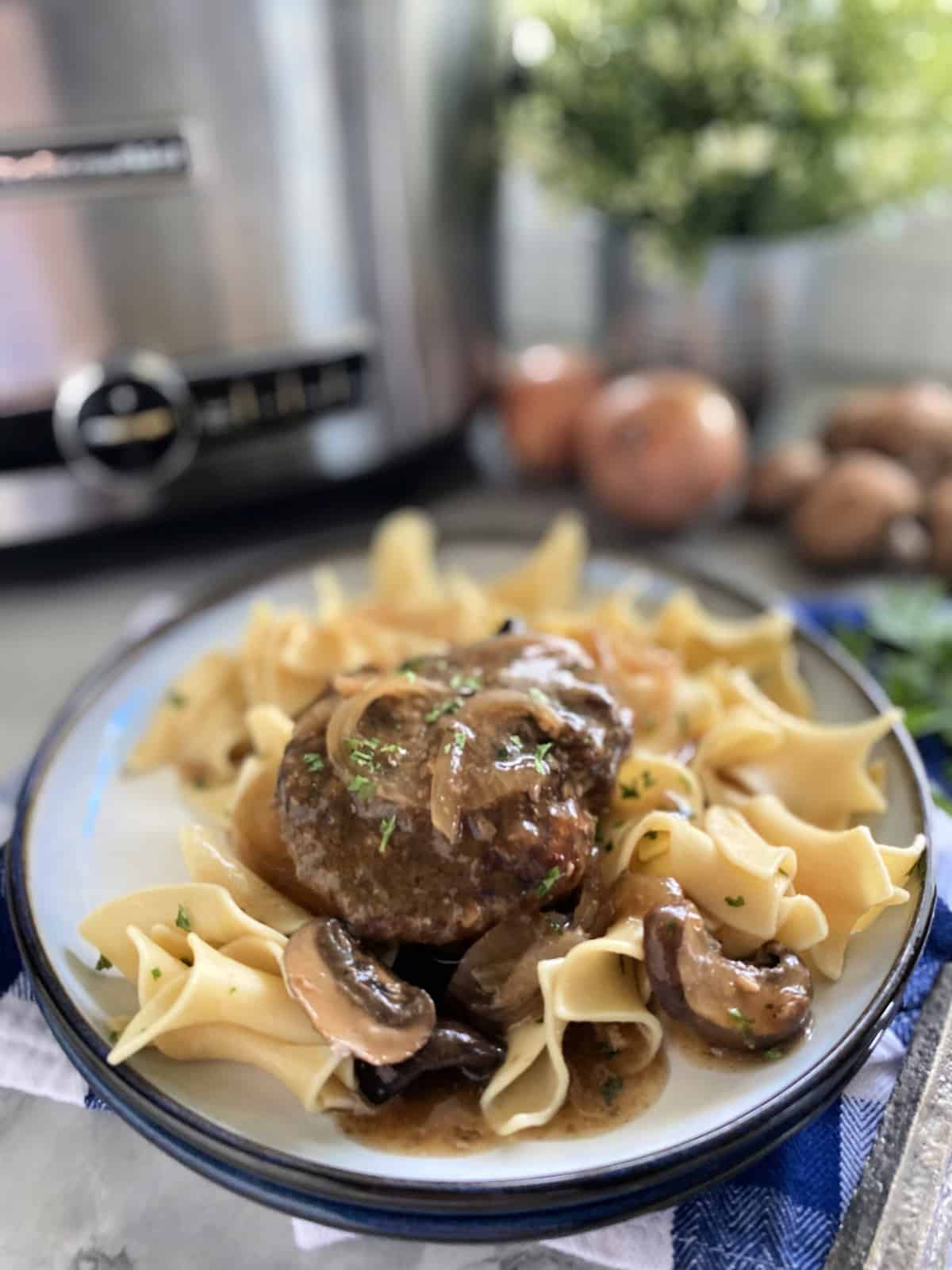 White plate with a blue rim filled with egg noodles, beef steak, and onion gravy.