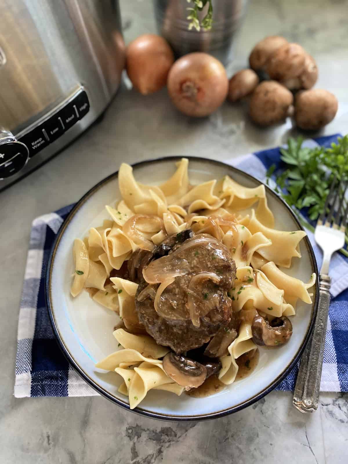 Top view of a white plate filled with egg noodles and a beef patty with mushrooms.