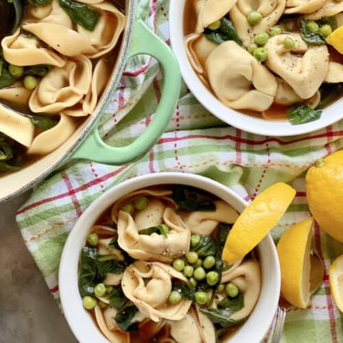 Top view of two white bowls and a green pot all filled with tortellini soup.