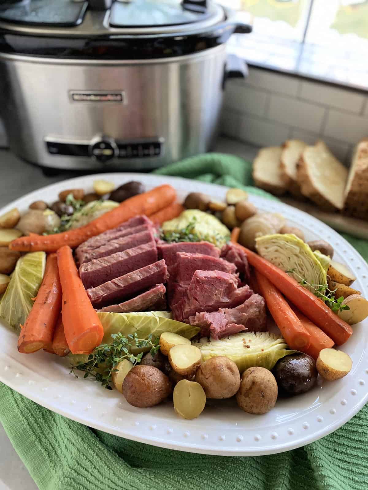 White platter filled with cabbage, corned beef, carrots, and slow cooker in the background.