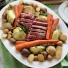 Top view of a white platter filled with meat and vegetables with plates and silverware on the side.
