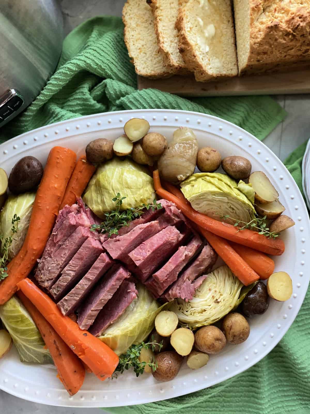 Top view of a white platter filled with beef, carrots, baby potatoes, and cabbage.