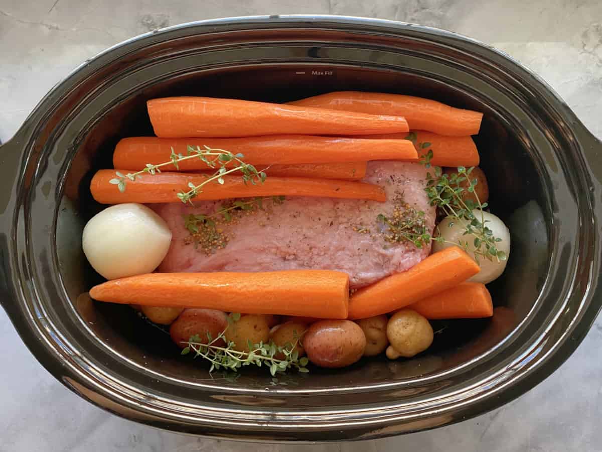 Top view of a slow cooker filled with carrots, onion, and beef.