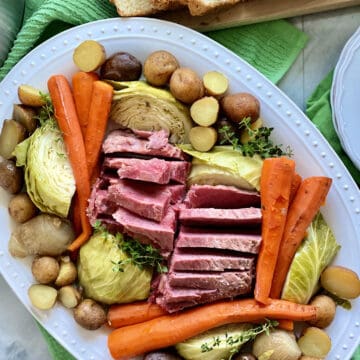 Top view of a white platter filled with beef, carrots, potatoes, and cabbage.