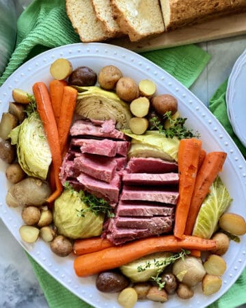 Top view of a white platter filled with beef, carrots, potatoes, and cabbage.