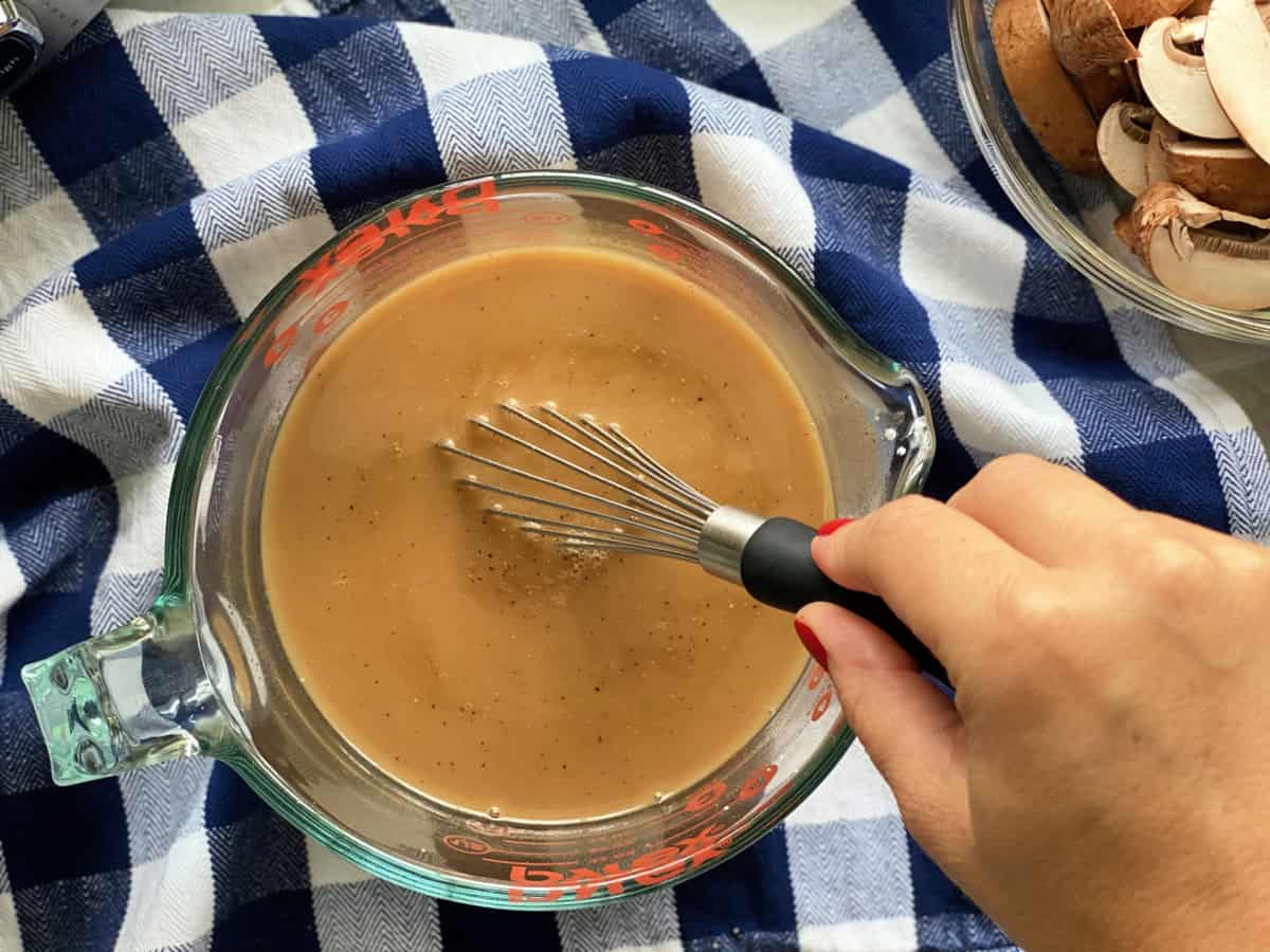 Female hand whisking brown liquid together in a glass measuring cup.