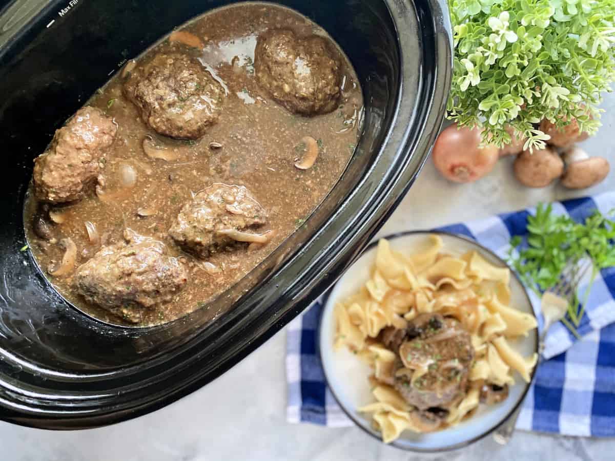 Top view of a slow cooker filled with gravy and steaks.