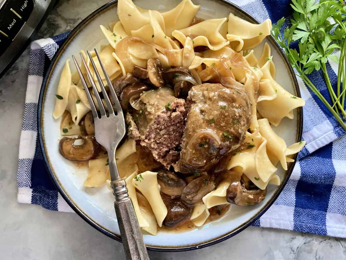 Top view of a meat steak cut in half sitting on top of noodles and gravy with a fork on top.