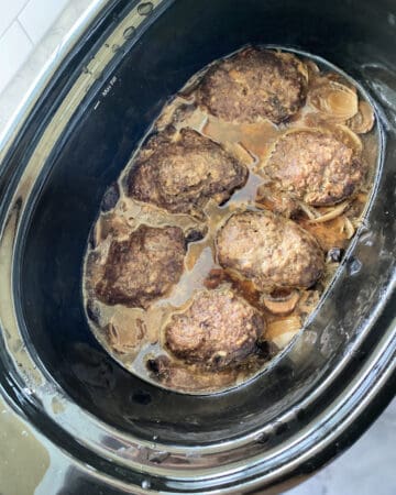 Top view of a black slow cooker filled with gravy and meat patties.