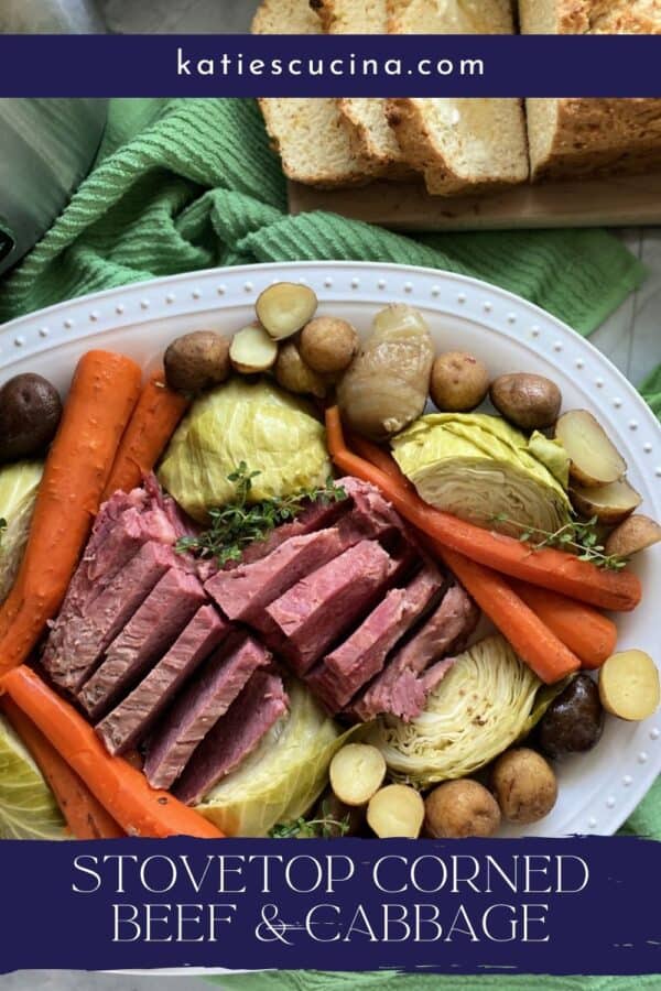 White platter filled with corned beef, cabbage, carrots, and potatoes with bread on the side.