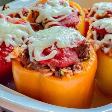 Yellow bell peppers in a white dish topped with tomato sauce and cheese.