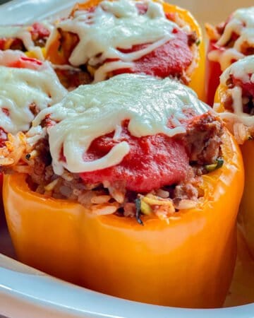 Yellow bell peppers in a white dish topped with tomato sauce and cheese.