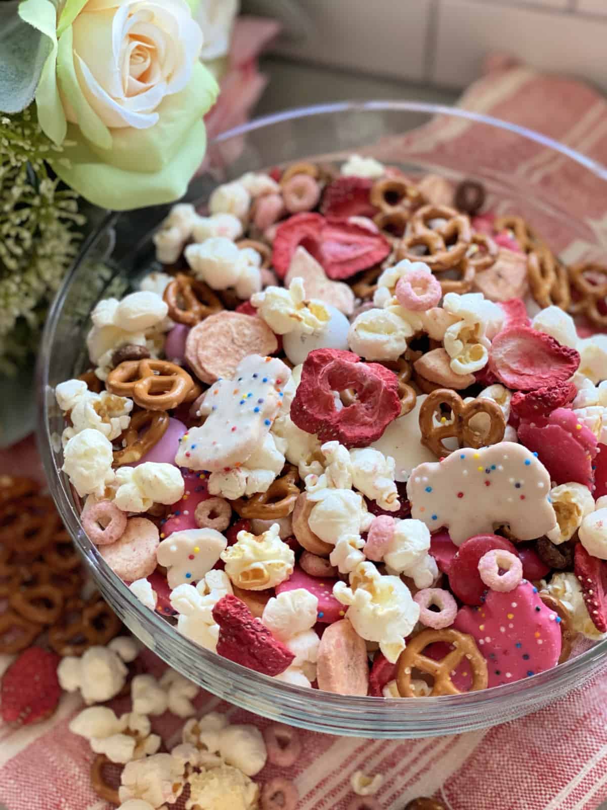 Glass bowl filled with red, white, and pink snacks with a flower next to it.