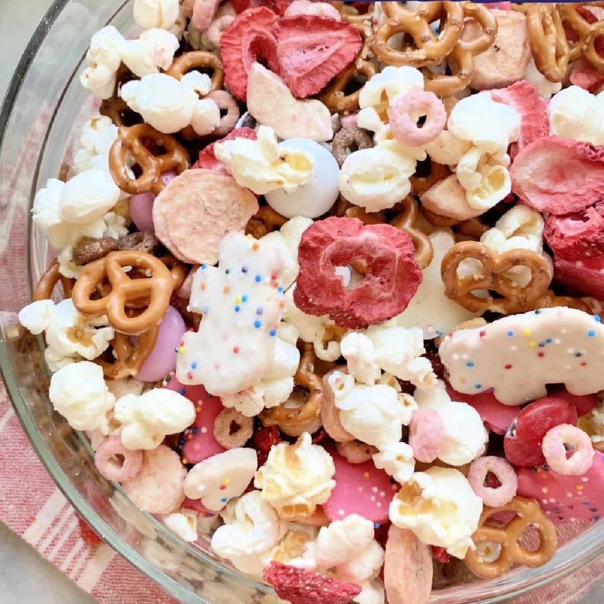 Pink and white snack mix with pretzels, dried strawberries, popcorn, and animal crackers.