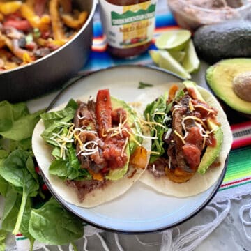 Two tacos on a plate with fajita peppers in the background.