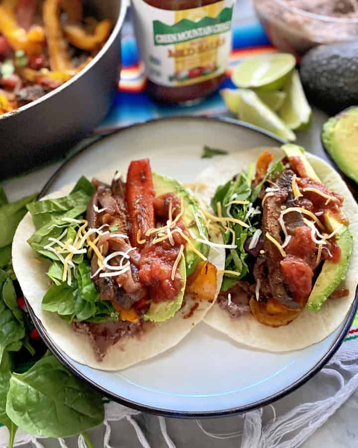 Two tacos on a plate with fajita peppers in the background.