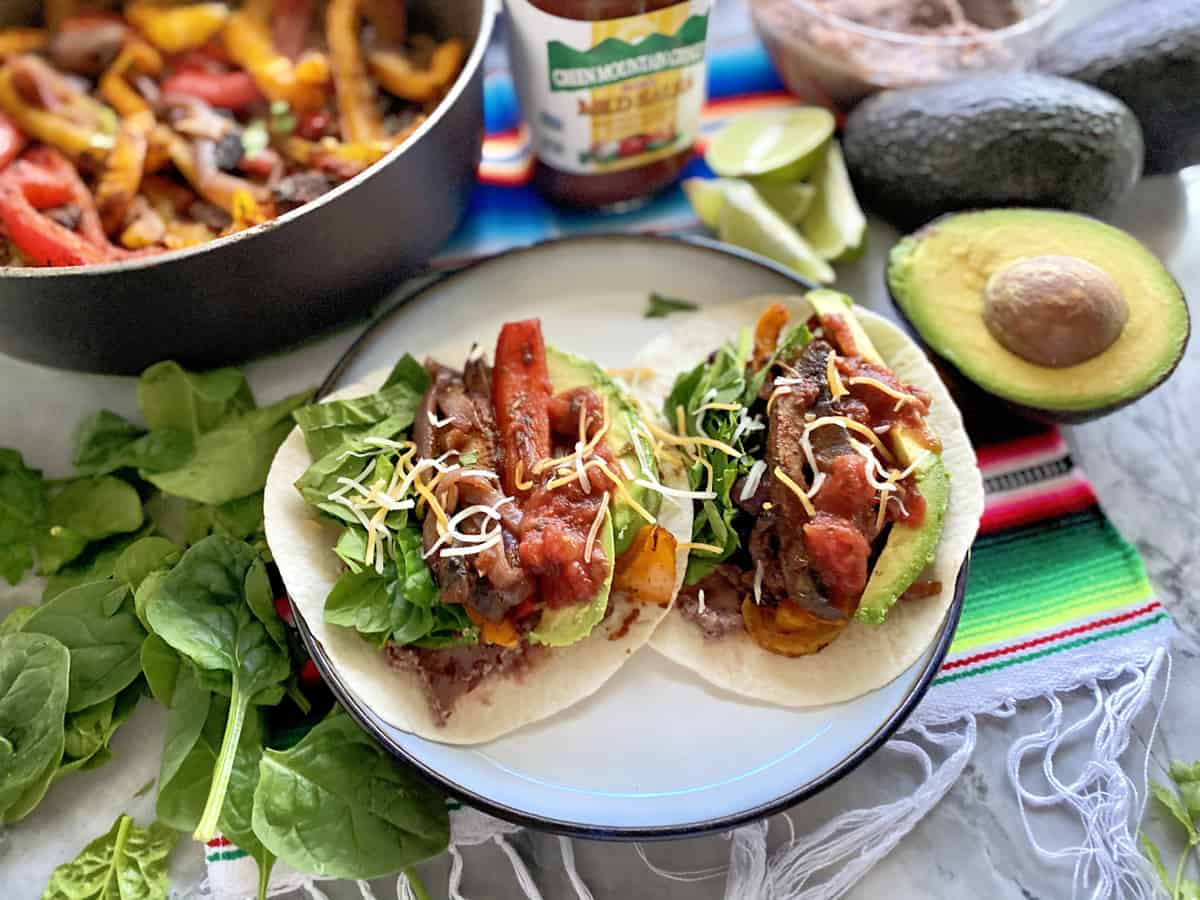 Two tacos on a plate with fajita peppers in the background.