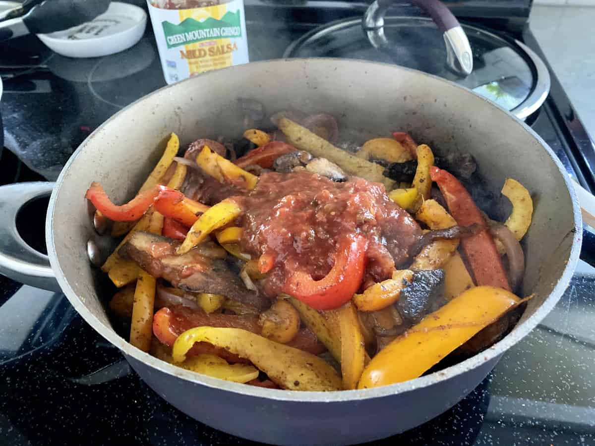 Brown skillet filled with cooked peppers and salsa on top.