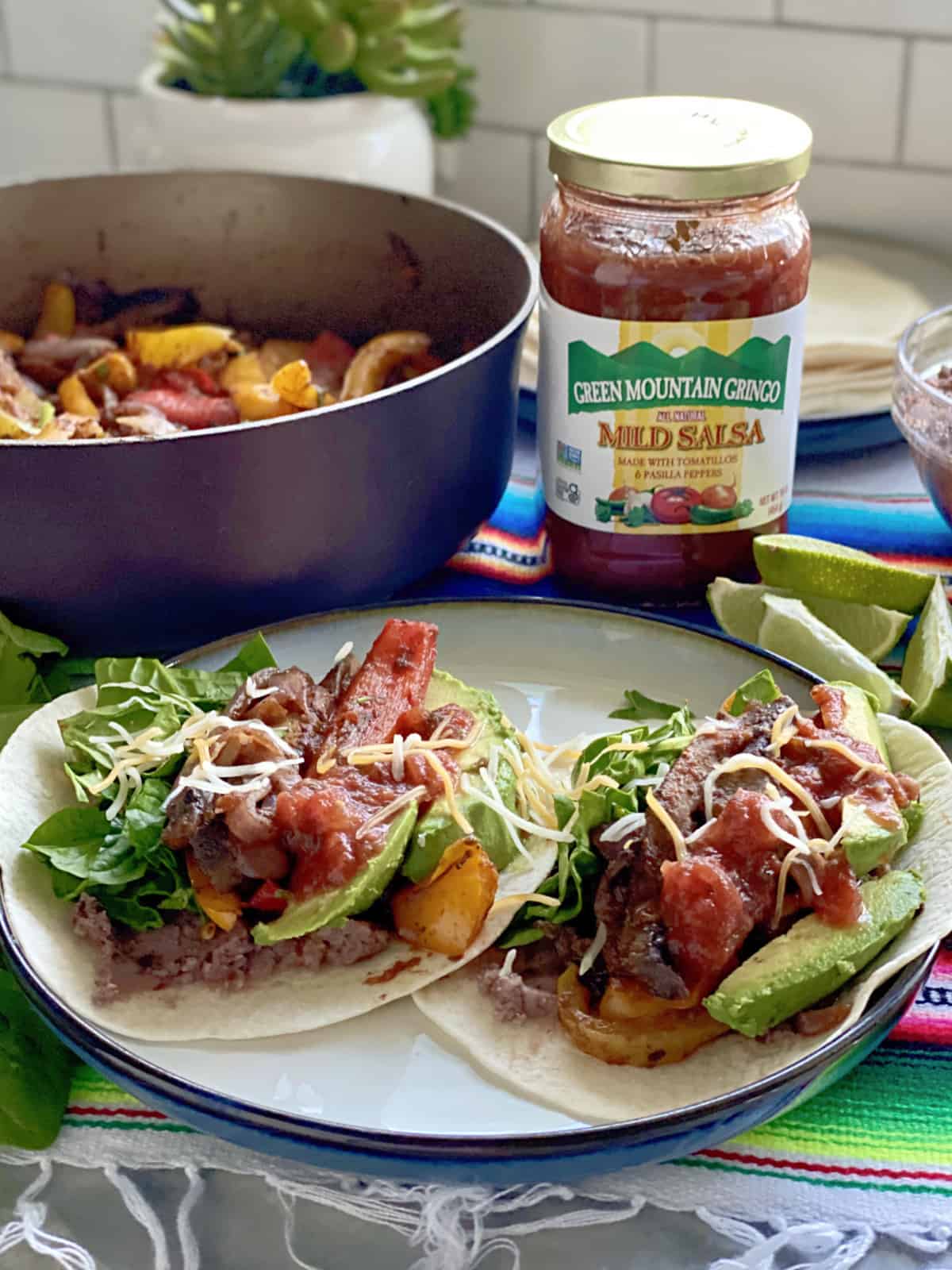 Two Vegetarian Fajitas with glass jar of salsa and skilelt in background.