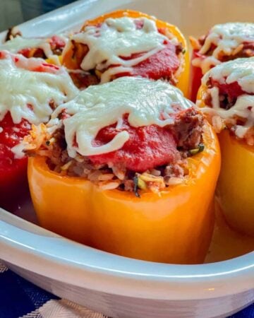 close up of orange stuffed peppers with red sauce and white cheese.