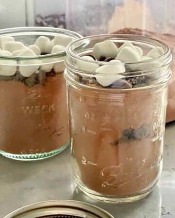 Two jars fileld with hot cocoa mix with container in the background.