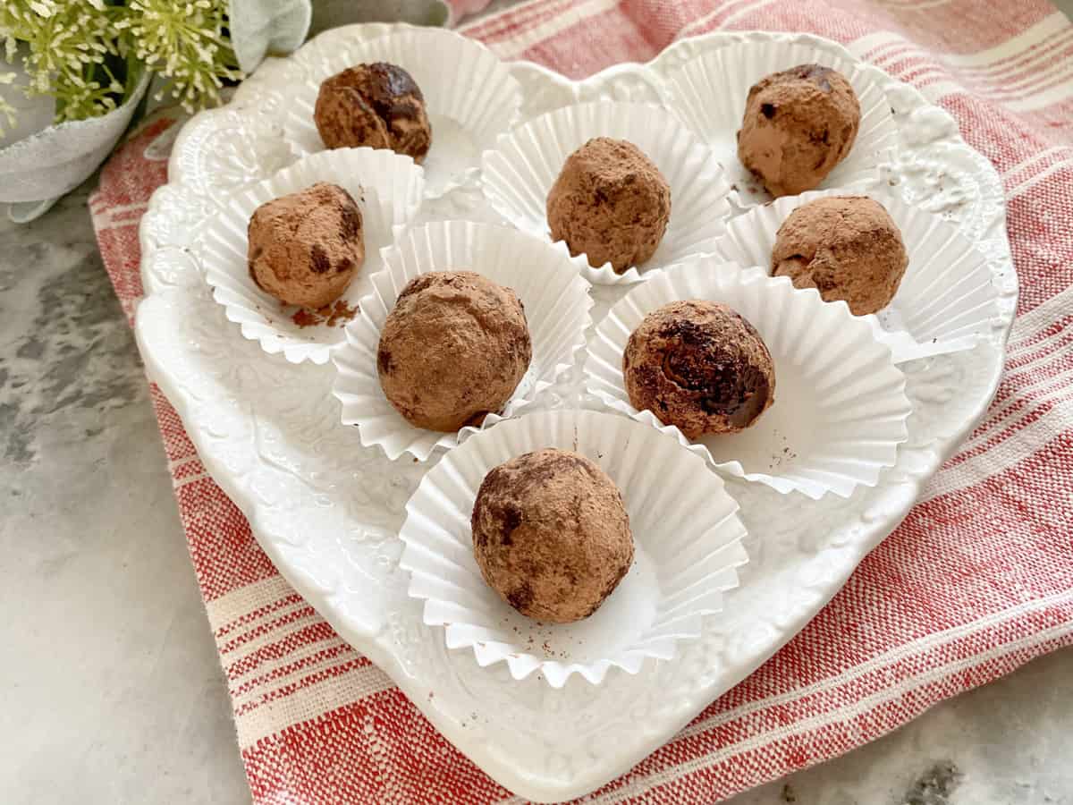 White heart shaped plate filled with 8 chocolate truffles.