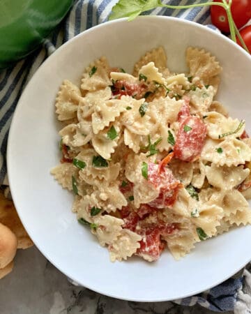 Top view of a white bowl of pasta filled with bow tie pasta and tomatoes.
