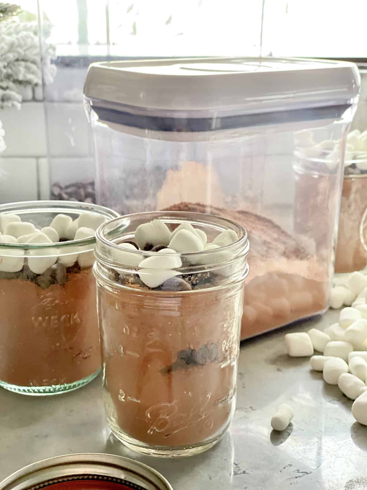 Two jars fileld with hot cocoa mix with container in the background.