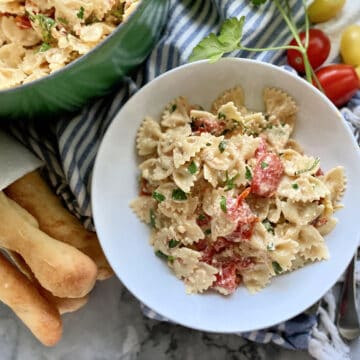 Top view of breadsticks, and a pot of pasta with a bowl next to it of creamy bowtie pasta.