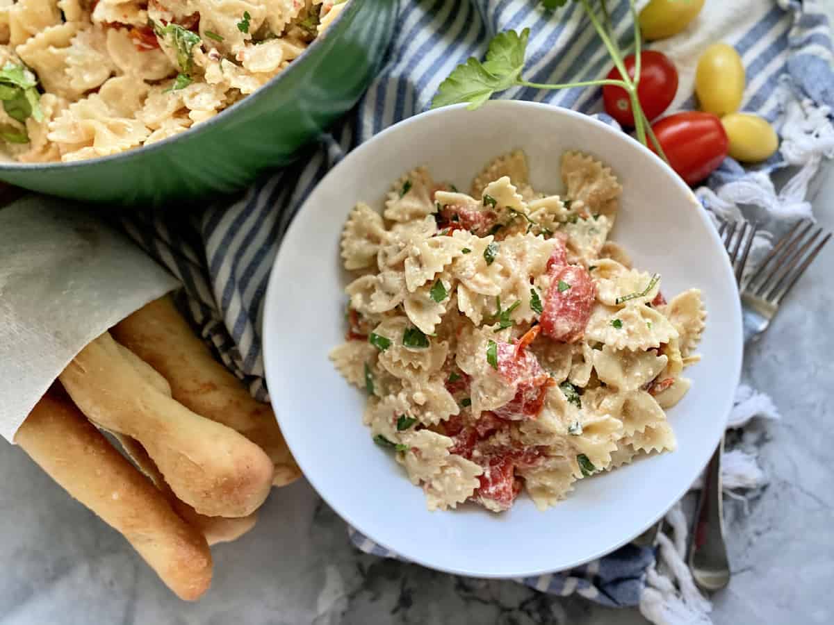 Top view of breadsticks, and a pot of pasta with a bowl next to it of creamy bowtie pasta.