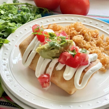 white plate with fried burrito topped with sour cream, gaucaumole, and diced tomatoes on top.