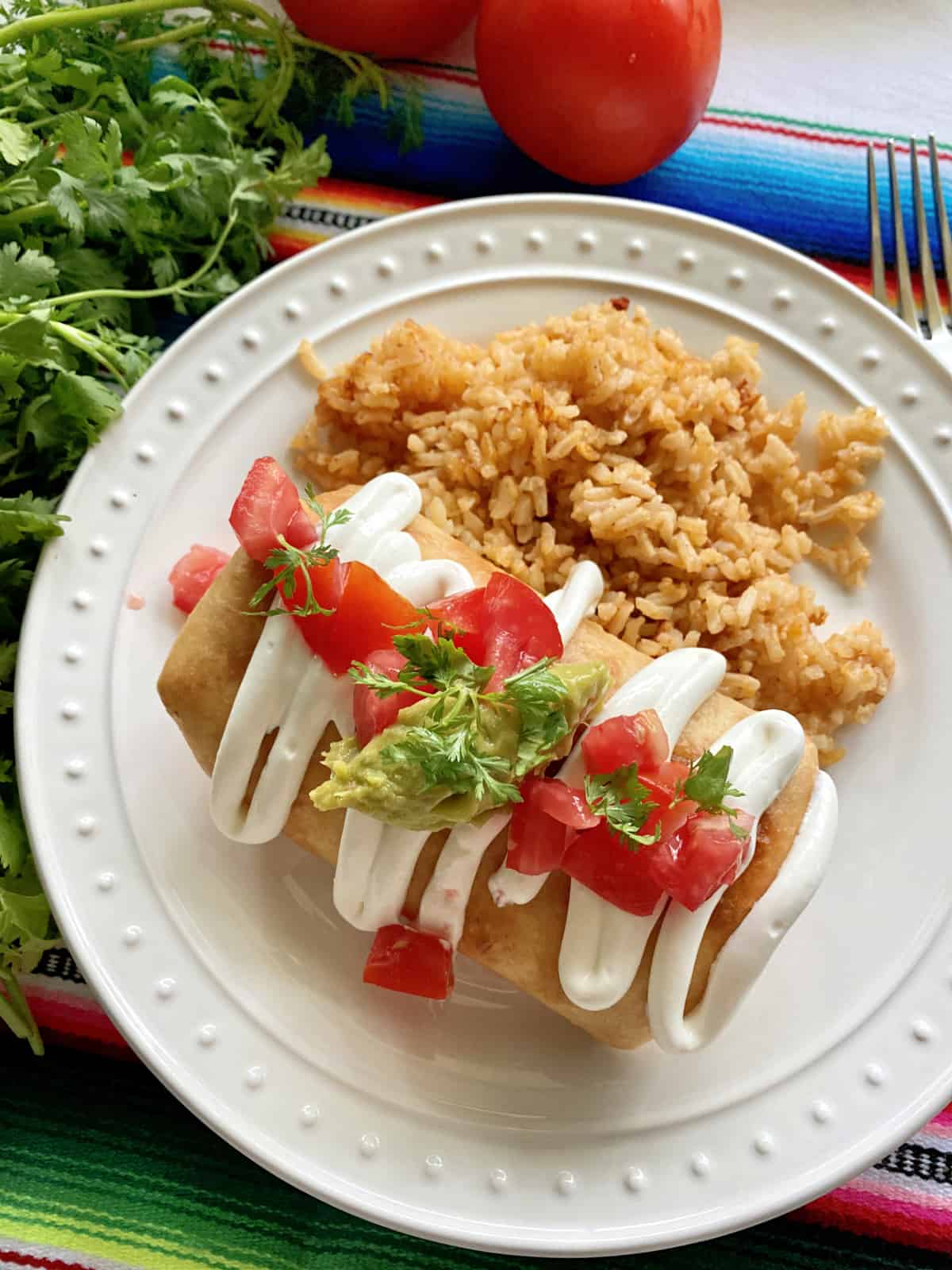 Top view of a white plate with a fried golden Chicken Chimichanga on the plate with toppings.