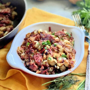 White dish filled with corned beef hash on a yellow cloth napkin.