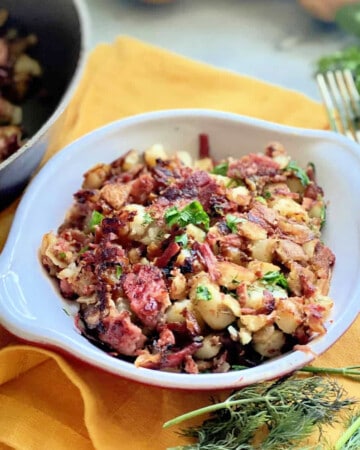 White dish filled with corned beef hash on a yellow cloth napkin.