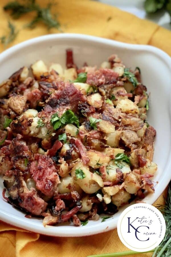 White plate filled with Corned Beef Hash and herbs with logo on right corner.