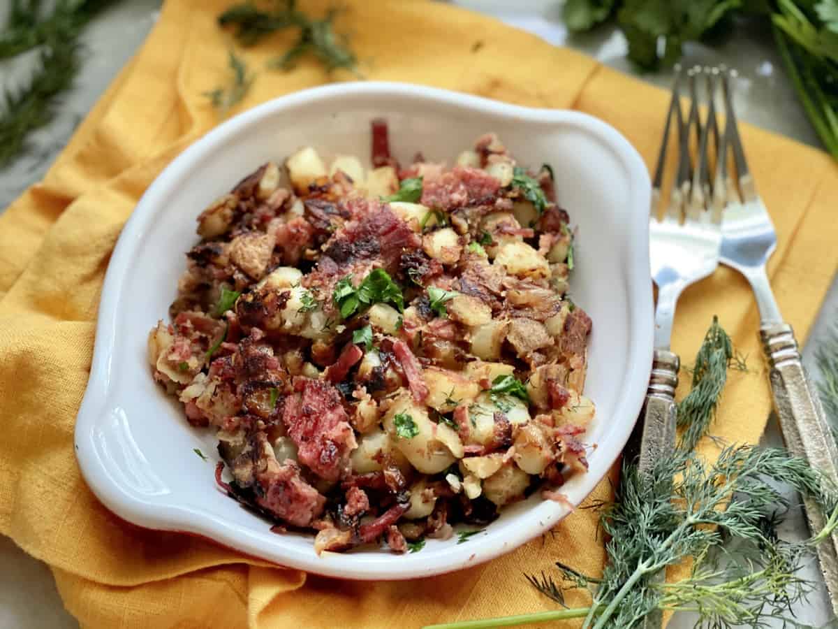 White shallow dish filled with corned beef and potatoes on a yellow napkin.