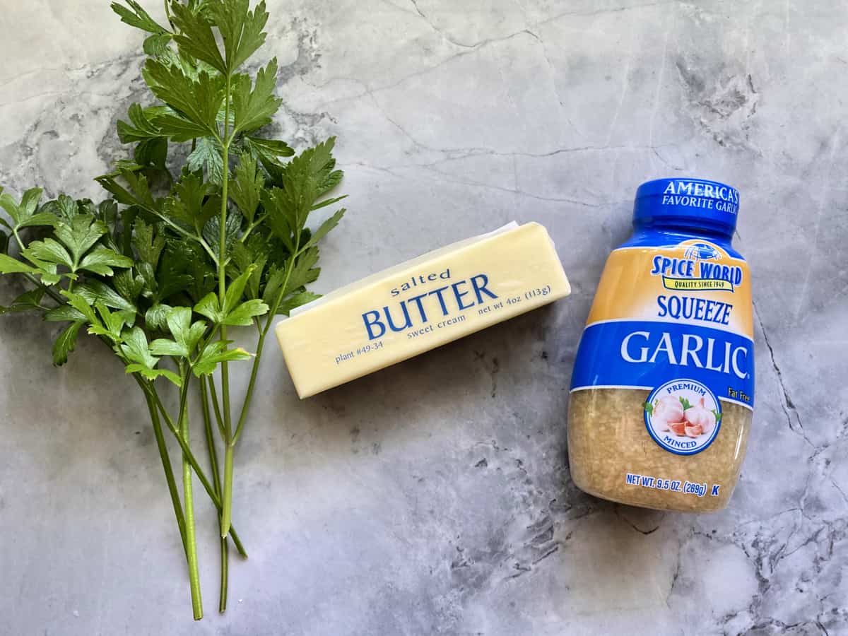 Ingredients on marble countertop: butter, garlic, and parsley.