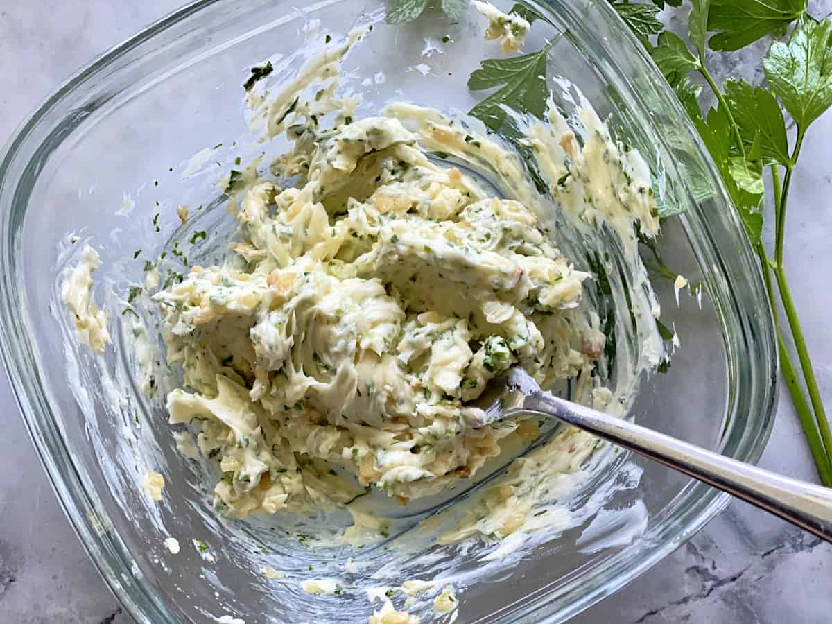 Square glass bowl filled with butter mixture and a fork burried under butter.