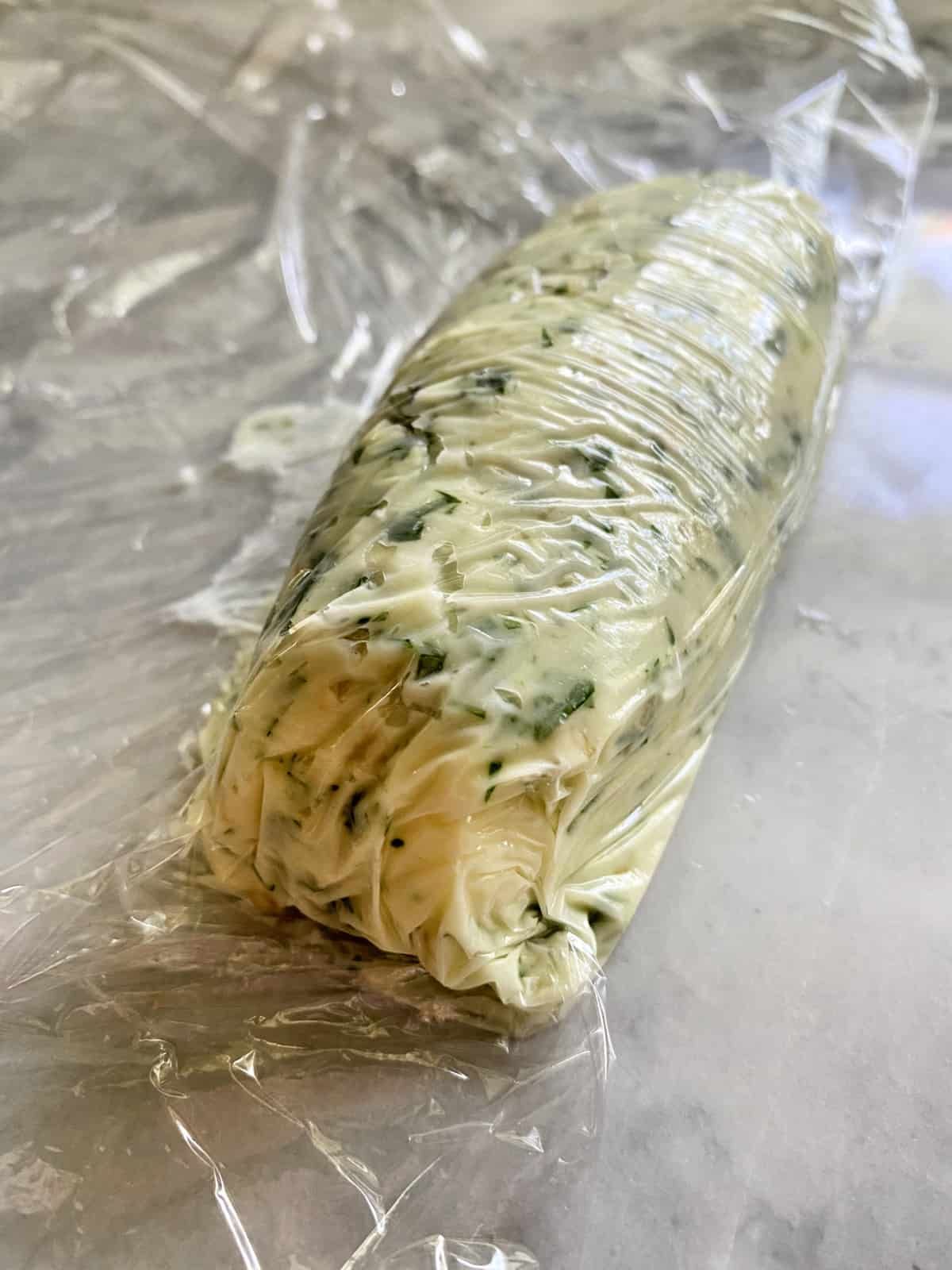 Close up of a log of Garlic Herb Butter wrapped in plastic wrap.